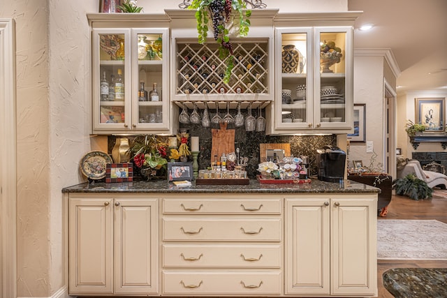 bar featuring tasteful backsplash, dark stone countertops, cream cabinetry, and ornamental molding