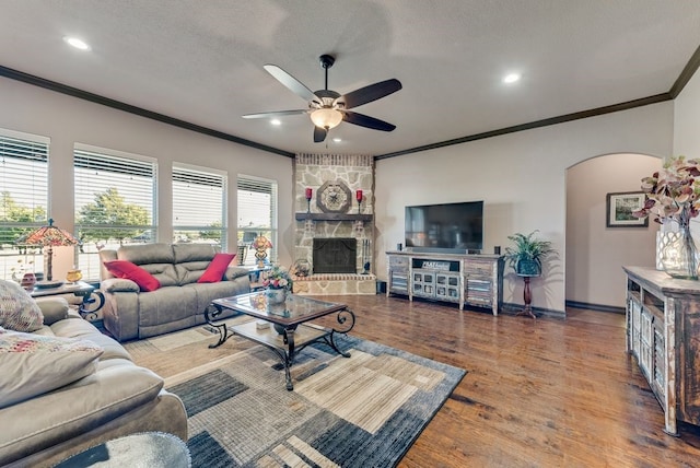 living room featuring arched walkways, ceiling fan, ornamental molding, wood finished floors, and a fireplace