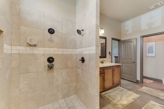 bathroom with vanity, a tile shower, visible vents, and baseboards