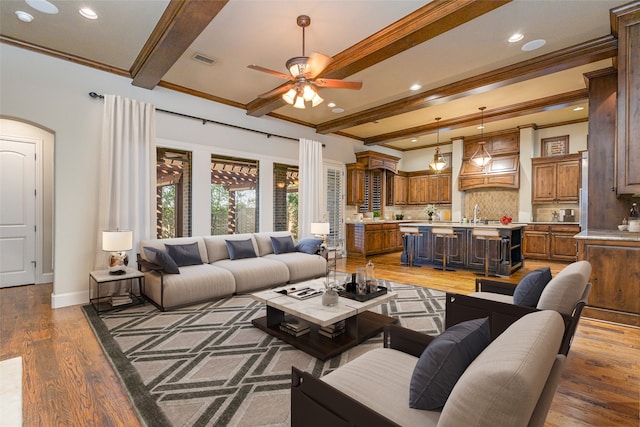 living room featuring beamed ceiling, crown molding, ceiling fan, and dark wood-type flooring