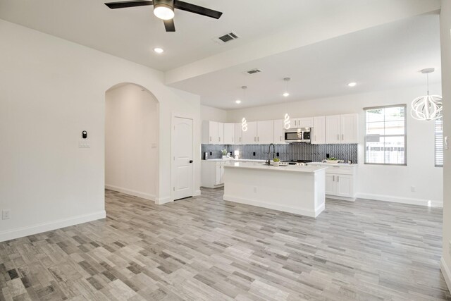 kitchen featuring light wood-type flooring, a kitchen island with sink, ceiling fan, pendant lighting, and white cabinets