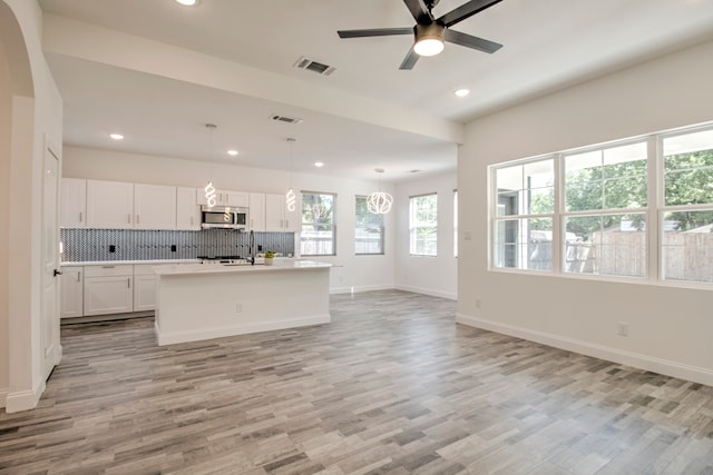 kitchen featuring light hardwood / wood-style flooring, pendant lighting, a kitchen island with sink, white cabinets, and ceiling fan with notable chandelier