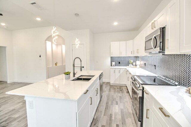 kitchen with white cabinetry, sink, hanging light fixtures, stainless steel appliances, and a kitchen island with sink