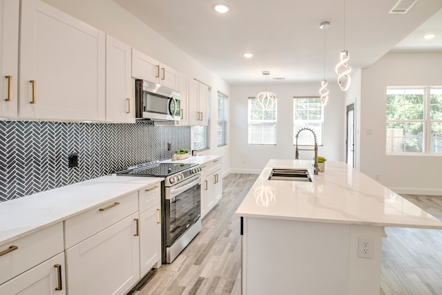 kitchen featuring pendant lighting, stainless steel appliances, a center island with sink, and light hardwood / wood-style floors