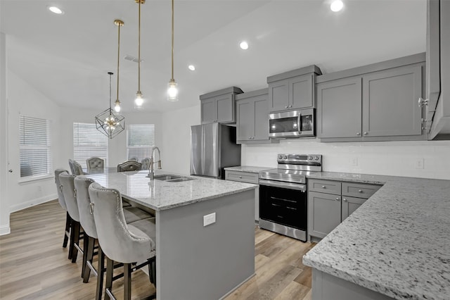 kitchen with light stone countertops, sink, hanging light fixtures, stainless steel appliances, and a kitchen island with sink