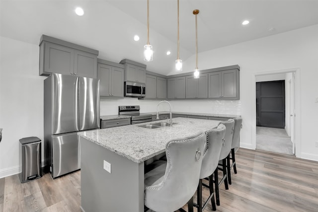 kitchen featuring sink, stainless steel appliances, light stone counters, pendant lighting, and a kitchen island with sink