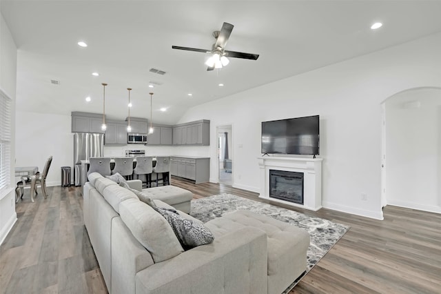 living room with ceiling fan, light hardwood / wood-style flooring, and vaulted ceiling