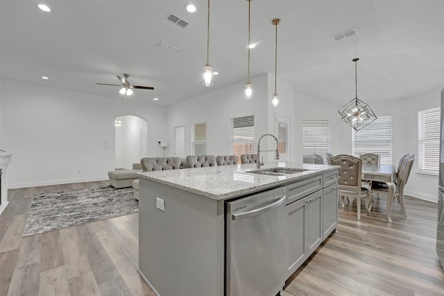 kitchen featuring light stone countertops, light hardwood / wood-style flooring, stainless steel dishwasher, an island with sink, and decorative light fixtures