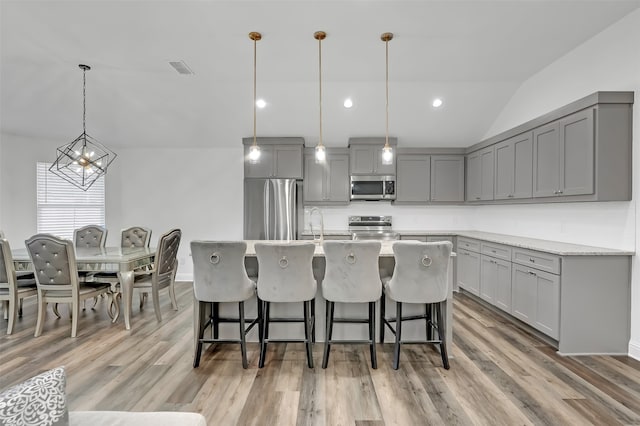 kitchen with light hardwood / wood-style flooring, gray cabinetry, vaulted ceiling, appliances with stainless steel finishes, and decorative light fixtures