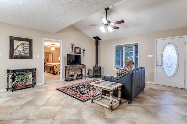 tiled living room with a textured ceiling, a wood stove, ceiling fan, and lofted ceiling