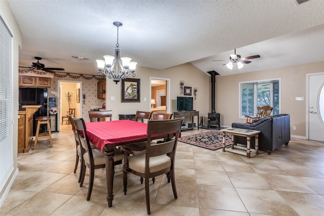 dining room with ceiling fan with notable chandelier, a wood stove, light tile patterned floors, and a textured ceiling