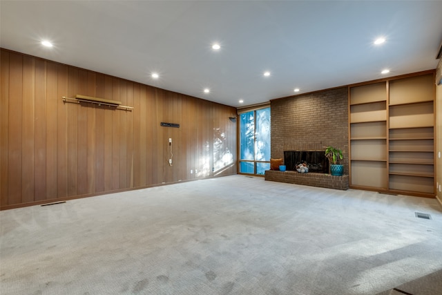 unfurnished living room with light colored carpet, a brick fireplace, and wood walls