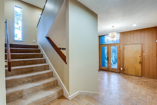 foyer featuring french doors, light parquet flooring, a notable chandelier, and wood walls