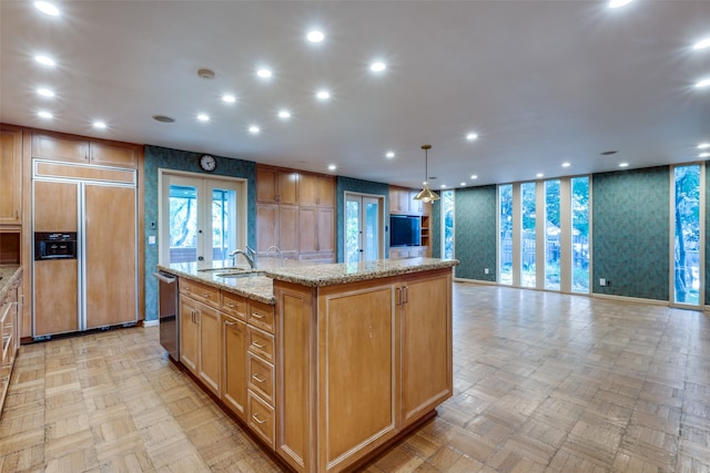 kitchen with a large island, paneled built in refrigerator, light parquet floors, and french doors