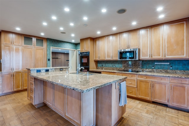 kitchen with light stone countertops, an island with sink, light parquet floors, and black appliances