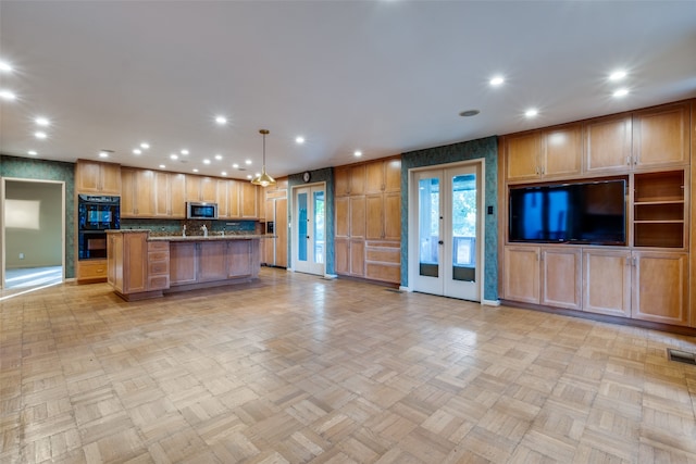 kitchen with stone counters, french doors, black double oven, decorative light fixtures, and a kitchen island with sink