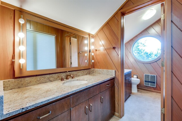 bathroom with wood walls, vanity, vaulted ceiling, and toilet