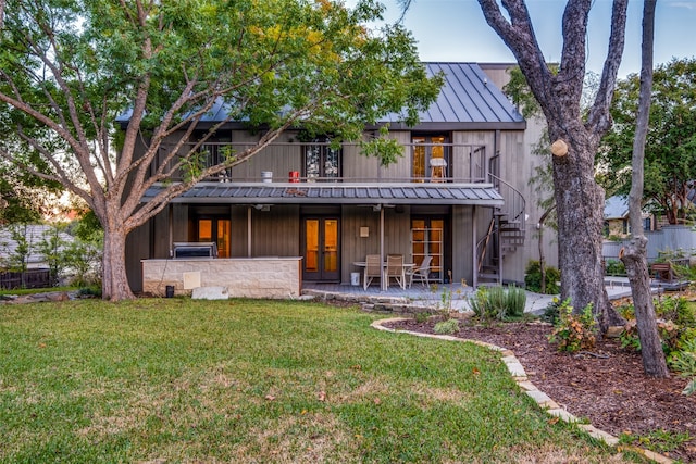 rear view of house with a lawn, a balcony, a patio, and french doors