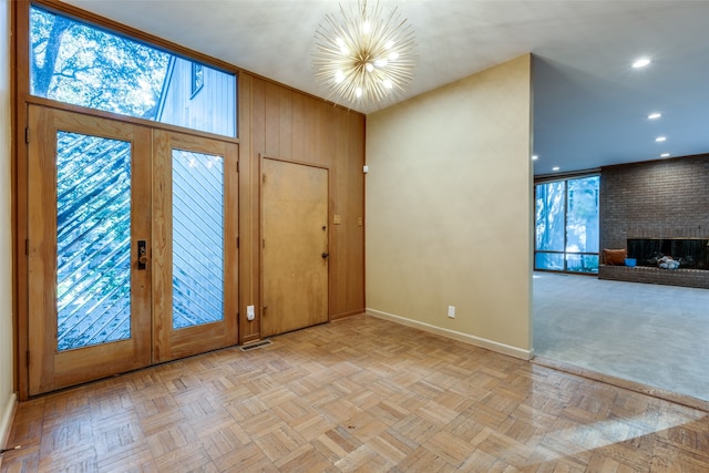 entrance foyer featuring french doors, an inviting chandelier, a brick fireplace, wooden walls, and light parquet flooring