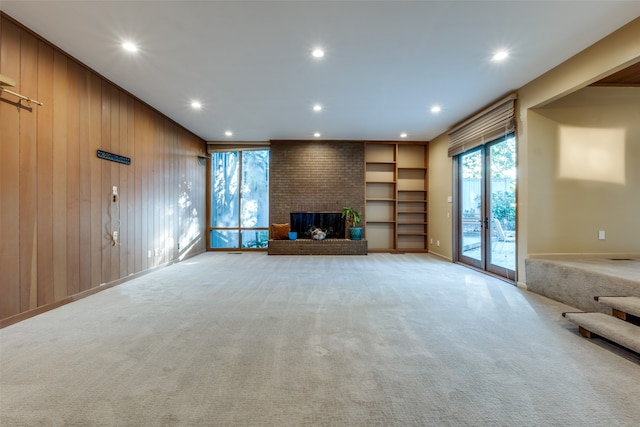 unfurnished living room with a brick fireplace, wood walls, and light carpet