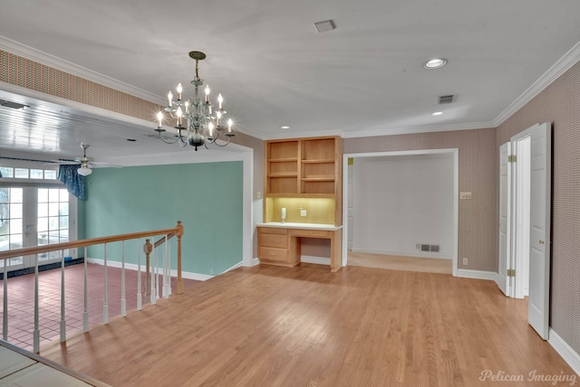 unfurnished room with ceiling fan with notable chandelier, built in desk, crown molding, and light hardwood / wood-style floors