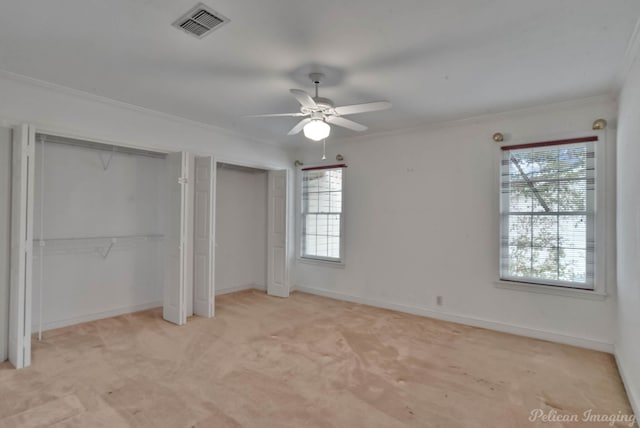 unfurnished bedroom with ceiling fan, crown molding, light colored carpet, and multiple closets