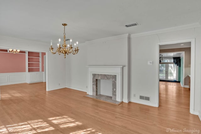 unfurnished living room with light hardwood / wood-style flooring, ornamental molding, a fireplace, built in shelves, and an inviting chandelier