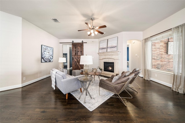 living room featuring dark wood-type flooring, ceiling fan, and a barn door