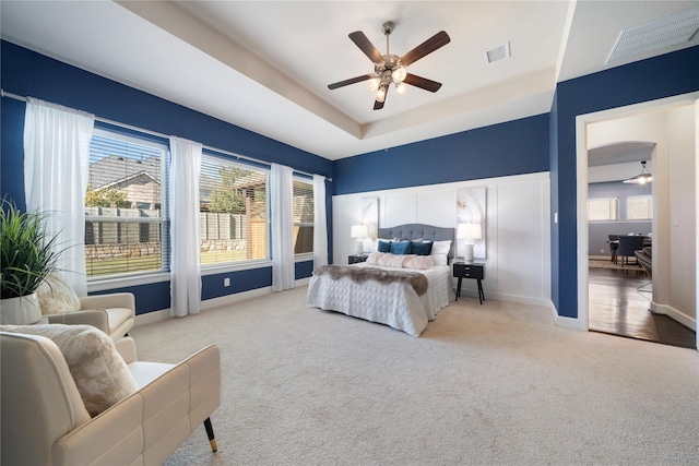 bedroom with ceiling fan, light colored carpet, connected bathroom, and a tray ceiling