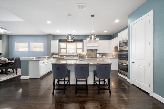 kitchen featuring stainless steel gas stovetop, a center island, white cabinetry, hanging light fixtures, and light stone counters