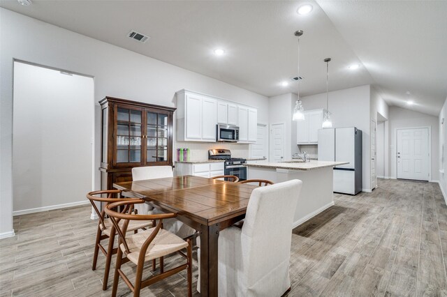 dining area with light wood-type flooring, lofted ceiling, and sink