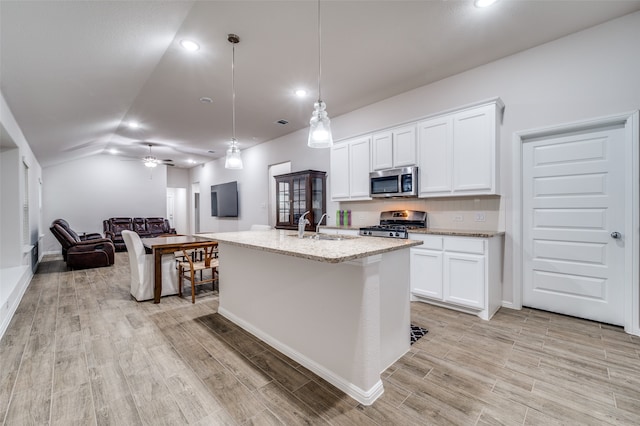 kitchen with stainless steel appliances, vaulted ceiling, pendant lighting, white cabinets, and an island with sink