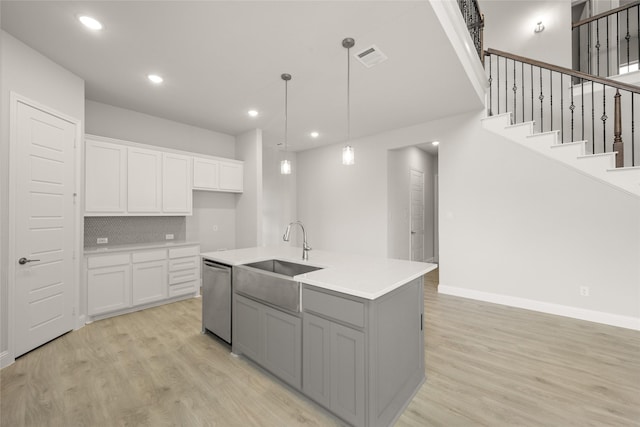 kitchen with light wood finished floors, dishwasher, white cabinetry, and a sink