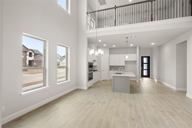 kitchen with baseboards, a center island with sink, stainless steel appliances, white cabinets, and light wood-style floors