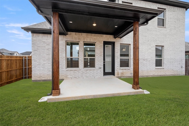 entrance to property with a patio area, fence, a lawn, and brick siding