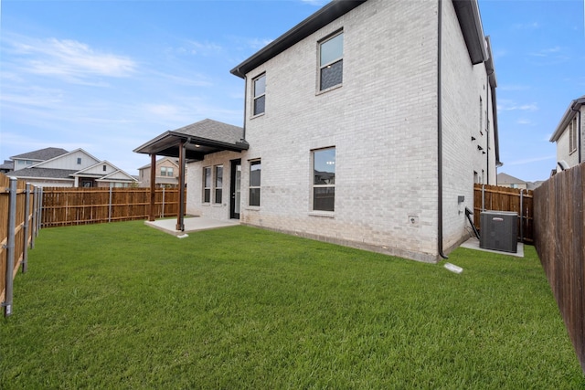 back of property with a fenced backyard, a lawn, brick siding, and central AC