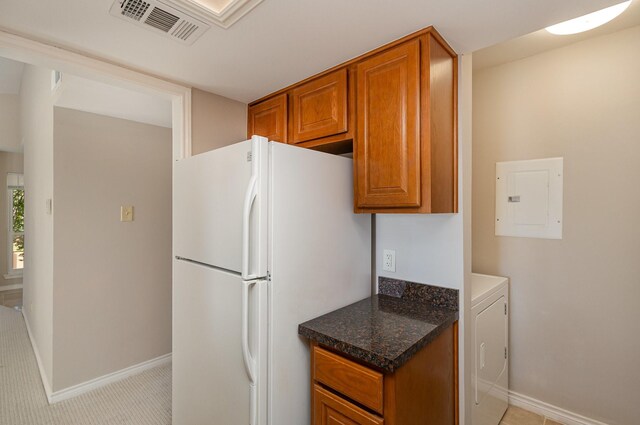 kitchen featuring light colored carpet, white refrigerator, dark stone countertops, washer / dryer, and electric panel