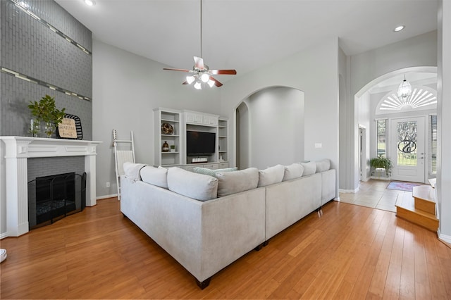 living room with wood-type flooring, ceiling fan with notable chandelier, high vaulted ceiling, and a brick fireplace