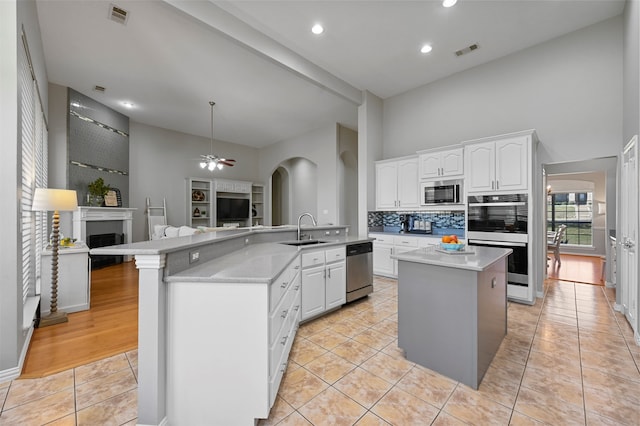 kitchen with kitchen peninsula, appliances with stainless steel finishes, sink, white cabinets, and a kitchen island