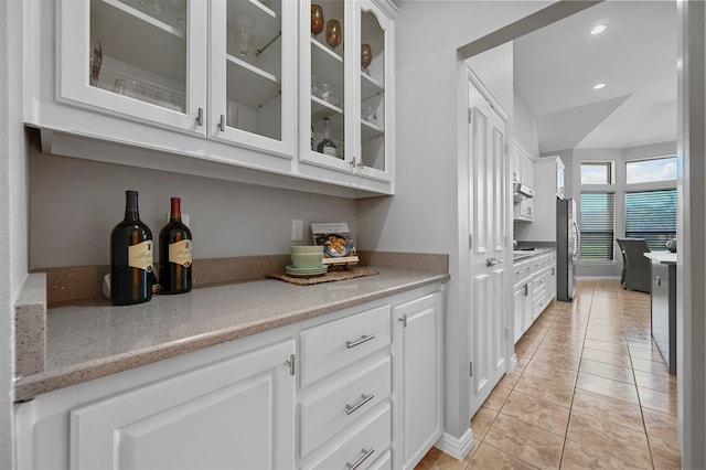 bar with stainless steel fridge, white cabinetry, and light tile patterned flooring