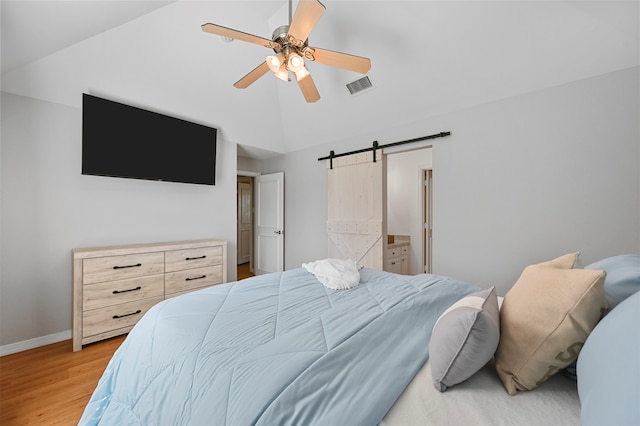 bedroom with ensuite bath, ceiling fan, a barn door, light hardwood / wood-style flooring, and lofted ceiling