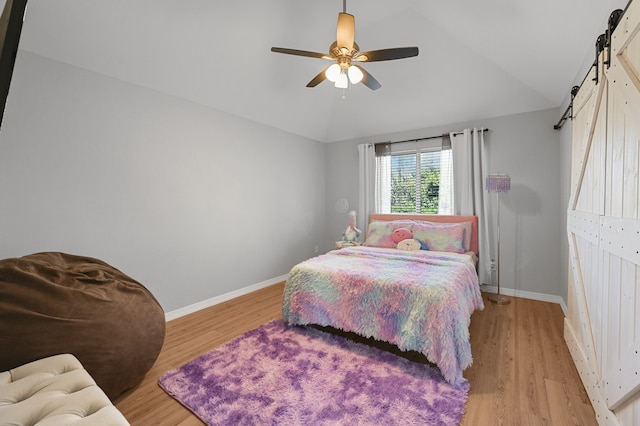 bedroom featuring light wood-type flooring, a barn door, ceiling fan, and lofted ceiling