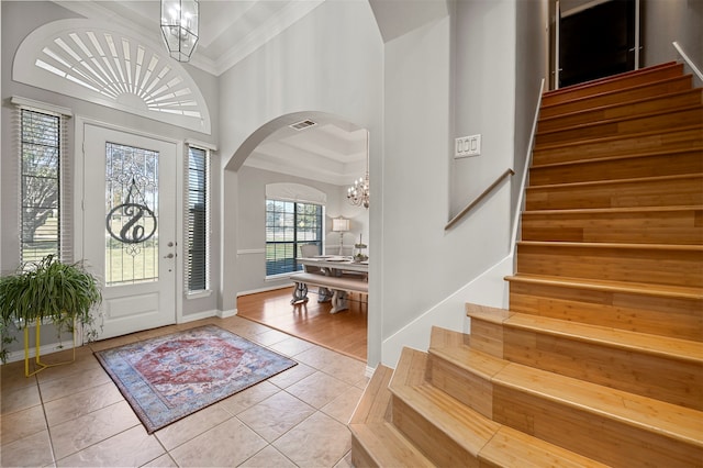 tiled entrance foyer with crown molding, a chandelier, and a high ceiling