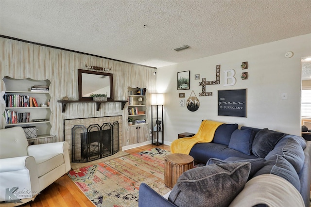 living area with a textured ceiling, a brick fireplace, wood finished floors, and visible vents