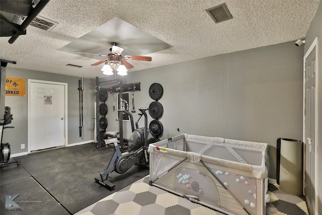 exercise room with a ceiling fan, visible vents, a textured ceiling, and baseboards