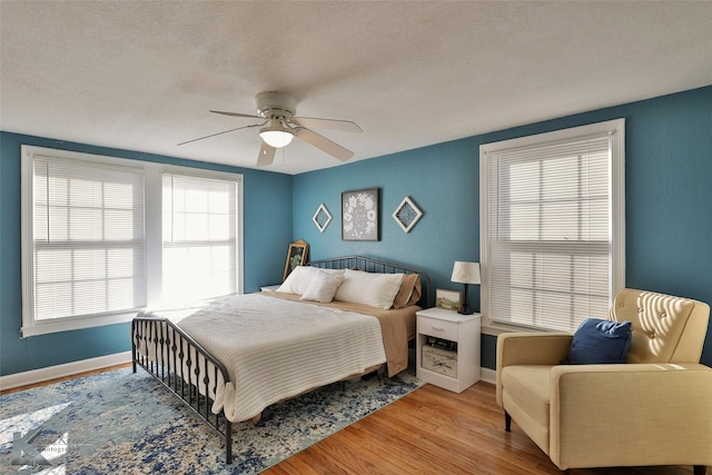 bedroom with light wood-style floors, a textured ceiling, baseboards, and a ceiling fan