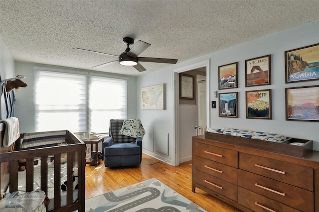 bedroom with ceiling fan, light hardwood / wood-style flooring, a nursery area, and a textured ceiling