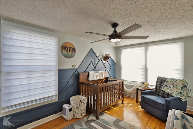 bedroom with hardwood / wood-style floors, a textured ceiling, a nursery area, and ceiling fan