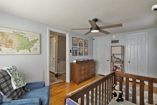 bedroom featuring a crib, ceiling fan, light hardwood / wood-style flooring, and a textured ceiling