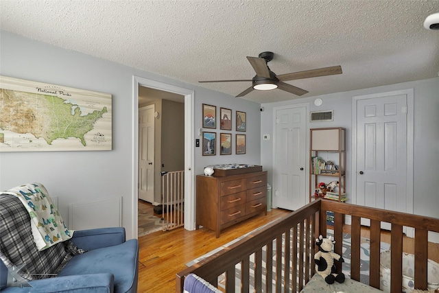 bedroom featuring a textured ceiling, ceiling fan, light wood finished floors, and visible vents